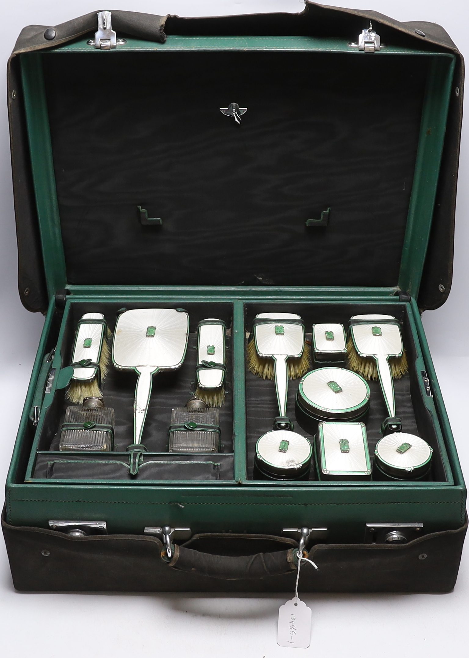 A George V silver, enamel and Chinese jadeite mounted twelve piece dressing table set, Goldsmiths & Silversmiths Co Ltd, Birmingham, 1936, housed in green leather travelling case, case width 53cm (a.f.).